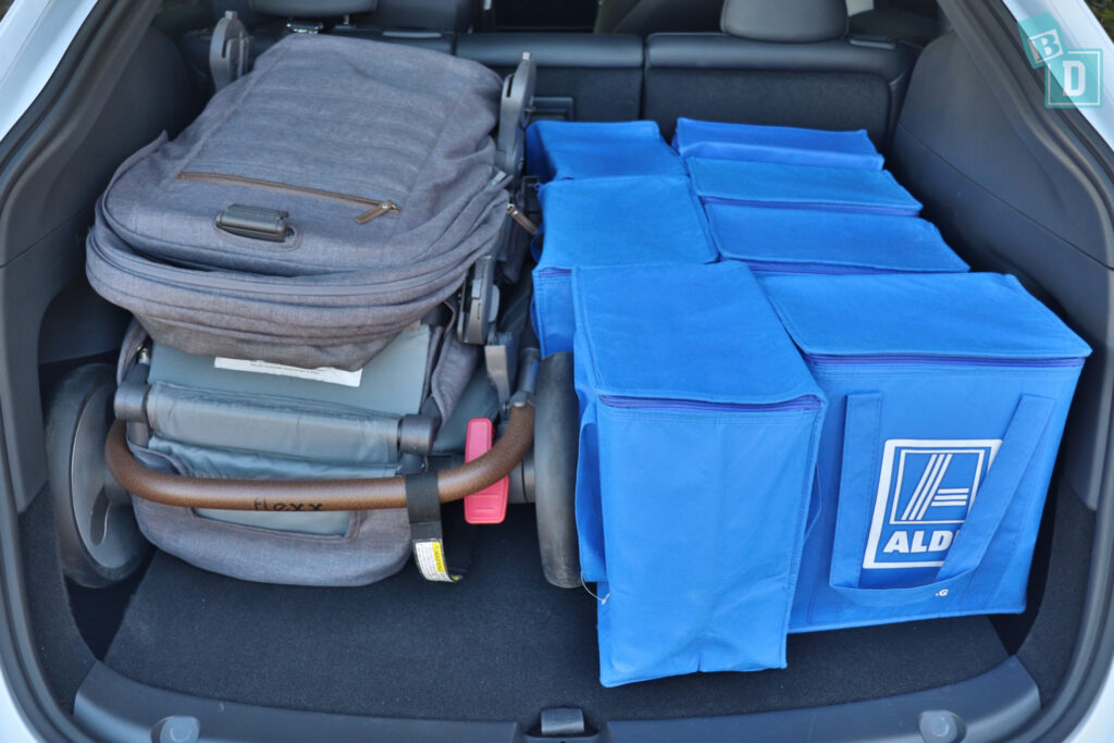 The trunk of a 2023 Tesla Model Y is filled with blue bags and a tandem stroller pram.