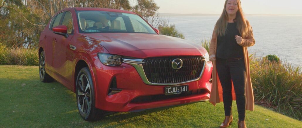 A woman presenting the 2023 Mazda CX-60 during its launch review, positioned beside a red SUV.