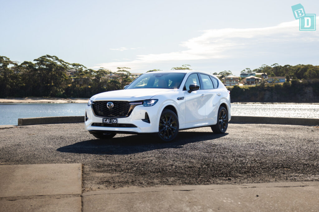 the white 2023 Mazda CX-60 is parked in front of a body of water.
