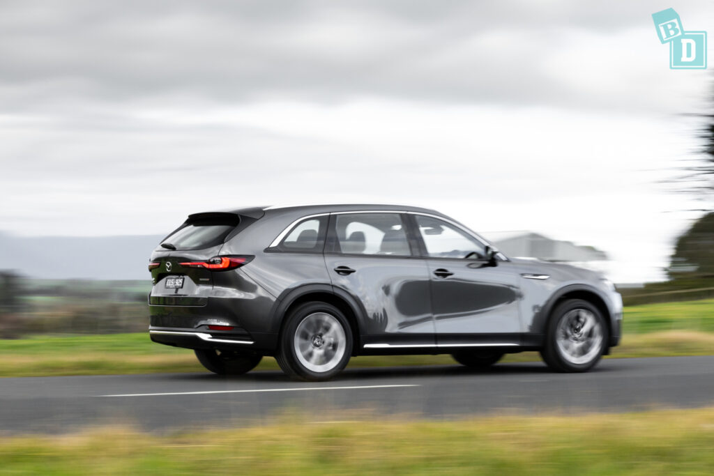 The 2023 mazda cx-90 is driving down a country road.