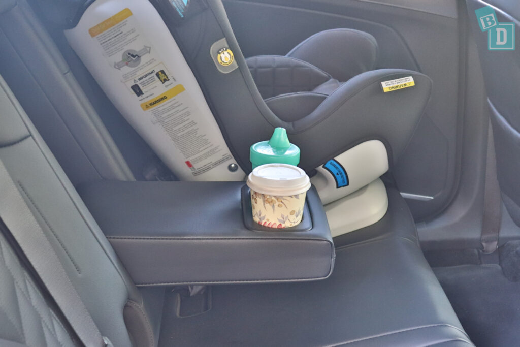 A baby in a car seat with a cup and a bottle.