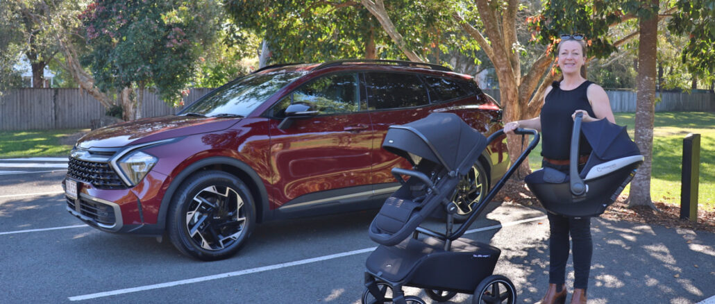 A woman standing next to a 2023 Kia Sportage with a baby stroller.