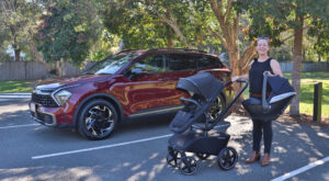 A woman standing next to a 2023 Kia Sportage with a baby stroller.