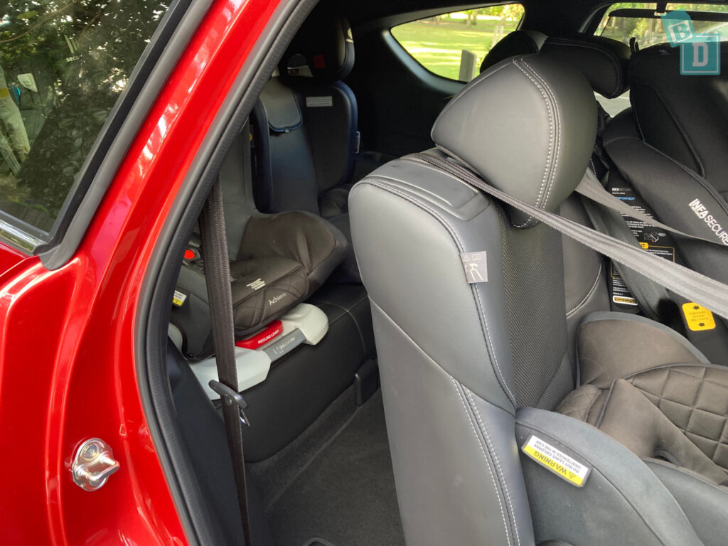 The back seat of a red car with two car seats.