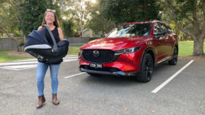 A woman standing next to a red Mazda CX-8 suv.