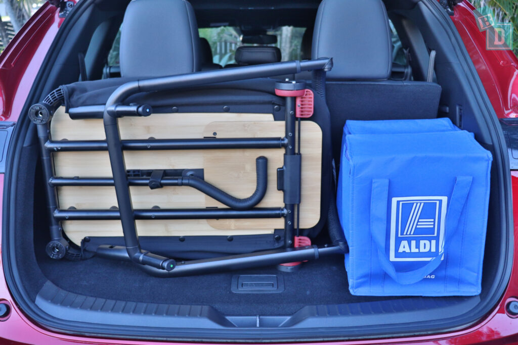 The trunk of a red car with a folding chair and a blue bag.